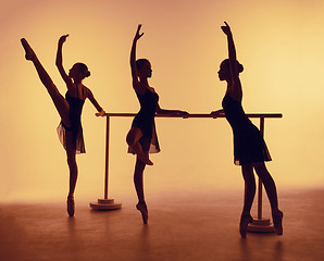 Image showing Composition from silhouettes of three young dancers in ballet poses on a orange background.