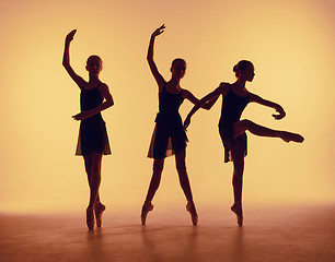 Image showing Composition from silhouettes of three young dancers in ballet poses on a orange background.