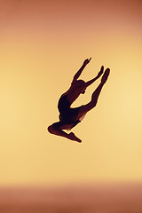 Image showing Beautiful young ballet dancer jumping on a orange background.