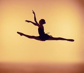 Image showing Beautiful young ballet dancer jumping on a orange background.