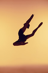 Image showing Beautiful young ballet dancer jumping on a orange background.