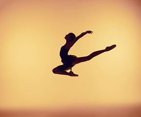 Image showing Beautiful young ballet dancer jumping on a orange background.