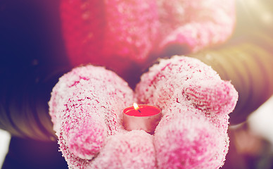 Image showing close up of hands in winter mittens holding candle