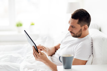 Image showing young man with tablet pc in bed at home bedroom