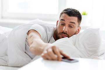 Image showing young man reaching for smartphone in bed