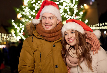 Image showing happy couple in santa hats at christmas tree