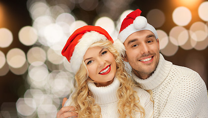 Image showing happy couple in santa hats over christmas lights