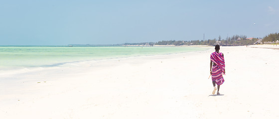 Image showing Maasai warrior walking on picture perfect tropical sandy beach. Paje, Zanzibar, Tanzania.