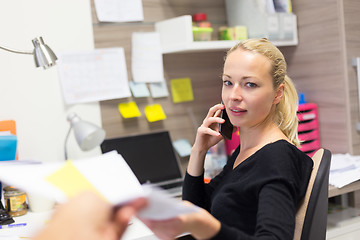 Image showing Business woman talking on mobile phone accepting papers.