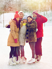 Image showing happy friends with smartphone on ice skating rink