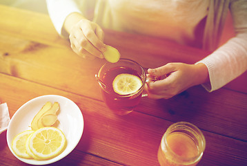 Image showing close up of woman adding ginger to tea with lemon