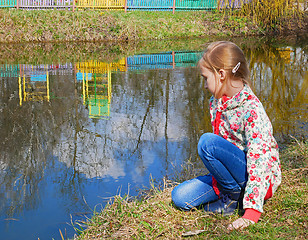 Image showing Small girl sits near the lake