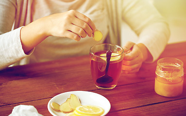 Image showing close up of woman adding ginger to tea with lemon