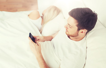 Image showing man texting message while woman is sleeping in bed