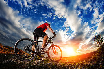 Image showing cyclist standing with mountain bike on trail at sunset