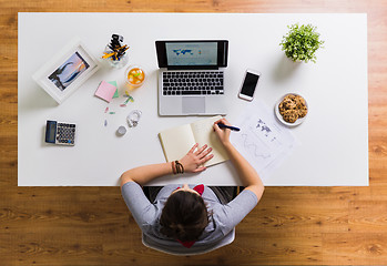 Image showing woman with laptop writing to notebook at office