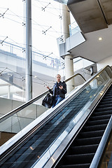 Image showing Businesswoman with large black bag and mobile phone descending on escalator.