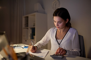 Image showing woman with calculator and papers at night office