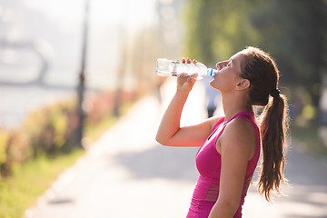 Image showing woman drinking water from a bottle after jogging