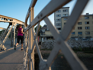 Image showing woman jogging across the bridge at sunny morning