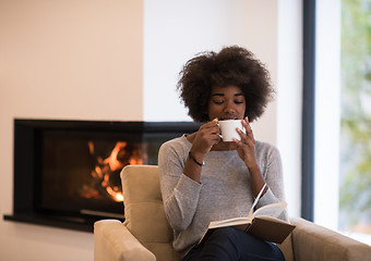 Image showing black woman reading book  in front of fireplace