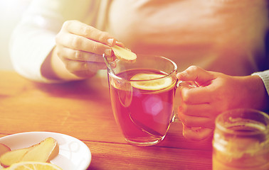 Image showing close up of woman adding ginger to tea with lemon