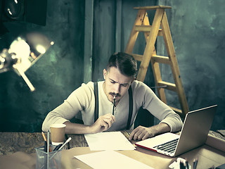 Image showing Portrait of a bearded businessman who is working with his notebook at loft studio.