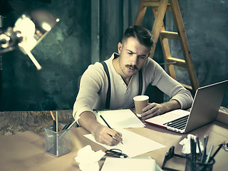 Image showing Portrait of a bearded businessman who is checking details of his upcoming meeting in his notebook and typing.