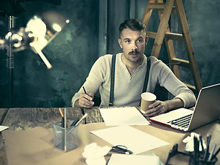 Image showing Portrait of a bearded businessman who is working with his notebook at loft studio.