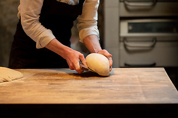 Image showing baker portioning dough with bench cutter at bakery