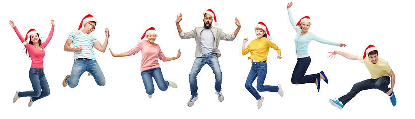 Image showing happy people in santa hats jumping in air