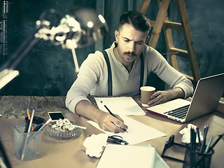 Image showing The handsome elegant man sitting at home table, working and using laptop while smoking cigarettes