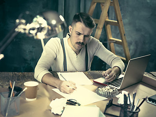 Image showing The handsome elegant man sitting at home table, working and using laptop while smoking cigarettes