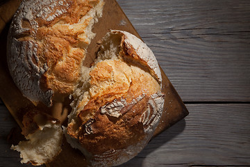 Image showing Torned homemade bread loaf on old cutting board with a free space on the right