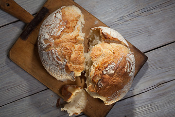 Image showing Torned homemade bread loaf on old cutting board with a free space on the right