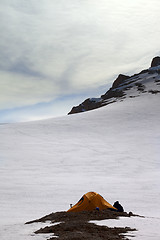 Image showing Hiker sitting near camping tent in evening snow mountains