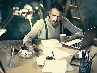 Image showing The handsome elegant man sitting at home table, working and using laptop while smoking cigarettes