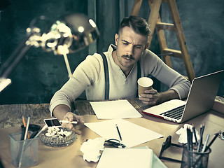 Image showing The handsome elegant man sitting at home table, working and using laptop while smoking cigarettes