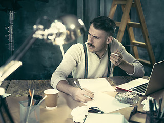 Image showing The handsome elegant man sitting at home table, working and using laptop while smoking cigarettes