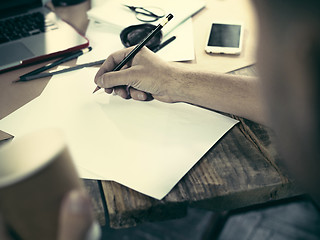 Image showing Vintage hipster wooden desktop side view, male hands with cup and holding a pencil