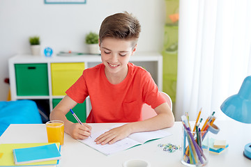 Image showing happy student boy writing to notebook at home