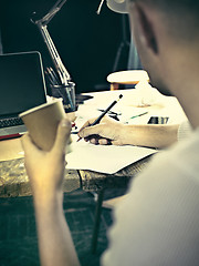 Image showing Vintage hipster wooden desktop side view, male hands with cup and holding a pencil