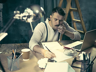 Image showing Portrait of a bearded businessman who is checking details of his upcoming meeting in his notebook and typing.