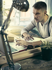 Image showing Portrait of a bearded businessman who is checking details of his upcoming meeting in his notebook and typing.