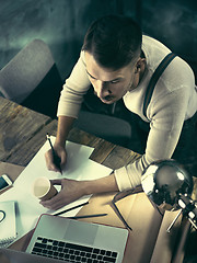 Image showing Vintage hipster wooden desktop top view, male hands using a laptop and holding a pencil