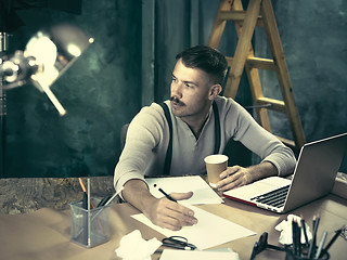 Image showing Portrait of a bearded businessman who is checking details of his upcoming meeting in his notebook and typing.