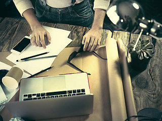 Image showing Vintage hipster wooden desktop top view, male hands using a laptop and holding a pencil