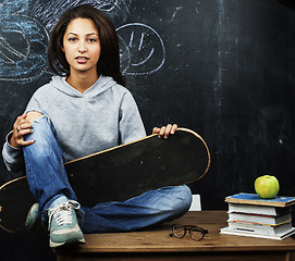 Image showing young cute teenage girl in classroom at blackboard seating on table smiling, modern hipster concept