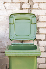Image showing Empty dirty green recycle bin near the brick wall