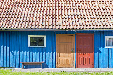 Image showing House of blue wooden planks, red roof, two colorful doors and small windows